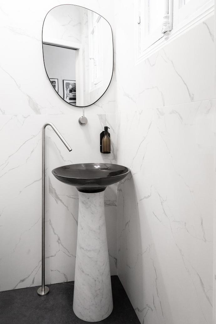 A Tamara freestanding washbasin from Riluxamade of Carrara marble and black resin in a white marble bathroom designed by Alak Studio