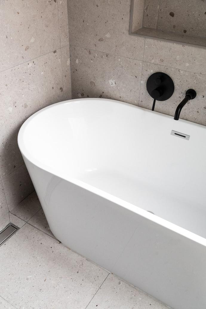 Closeup view of a white Bruges frestanding bath by Riluxa against terazzo tiles in a bathroom designed by Alak Studio